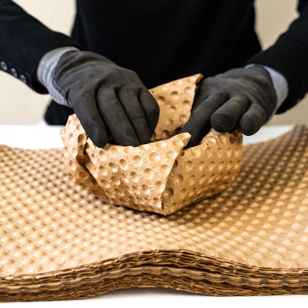 Hände in Handschuhen packen eine Schüssel in PapairSheets ein, damit sie geschützt ist. 