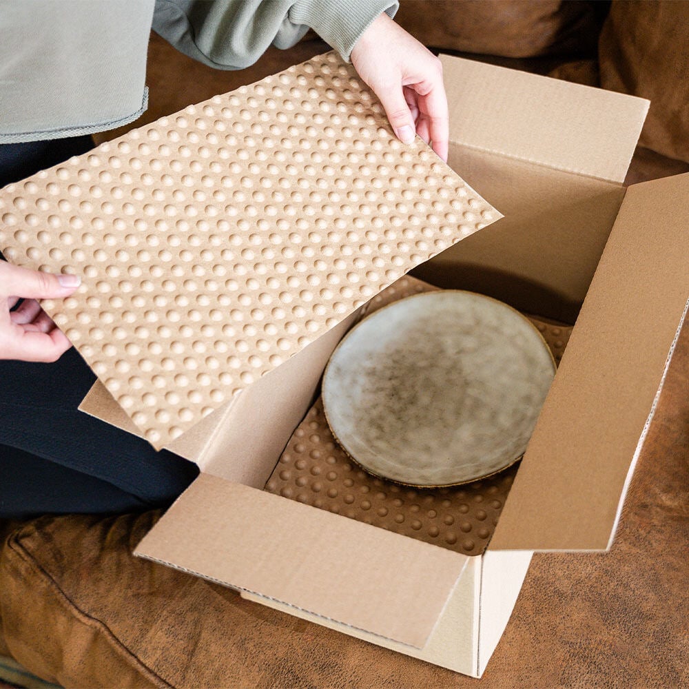 Eine Frau legt PapairSheets als Zwischenlage in ein Paket mit ihren Tellern, damit diese für den Umzug geschützt sind.