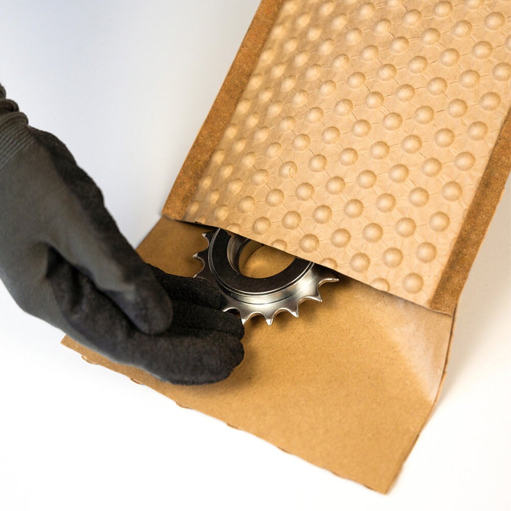 Eine Hand in einem Handschuh schiebt ein Zahnrad in einen beschichteten PapairBag.
