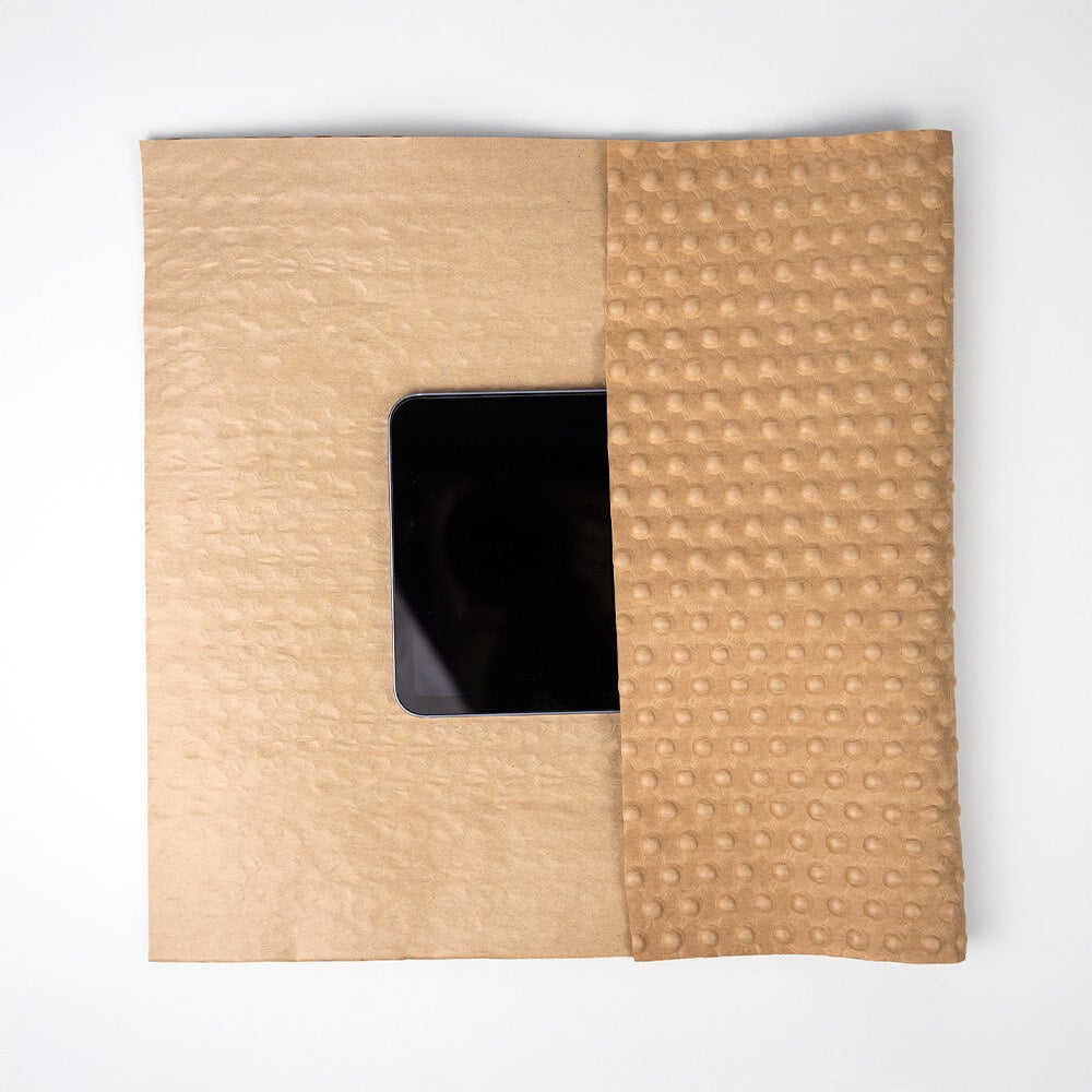 Ein Tablet liegt halb eingewickelt in einem Bogen beschichtetes PapairWrap Plus.