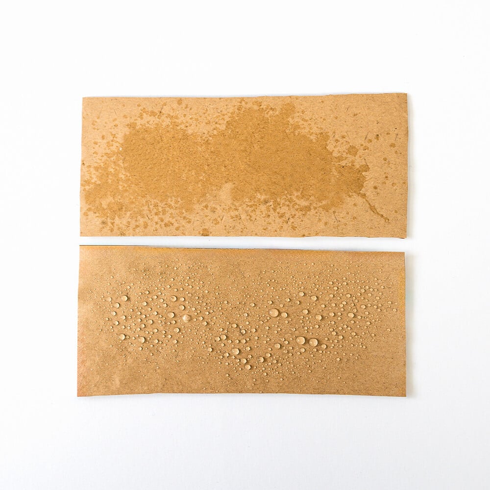 Zwei Stücke PapairWrap liegen übereinander für einen Vergleich von beschichtetem zu umbeschichtetem PapairWrap, beim beschichteten perlen die Wassertropfen ab, beim unbeschichteten zieht das Wasser ins Papier.